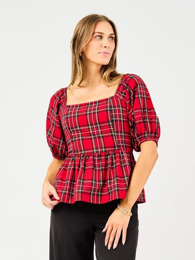 Woman wearing a red plaid top and black pants on a white background
