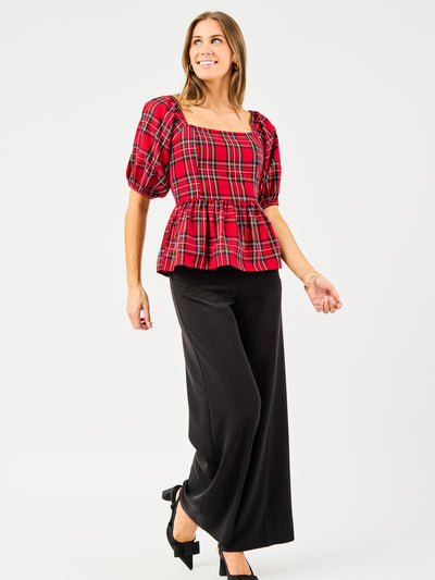 Woman wearing a red plaid top and black pants on a white background