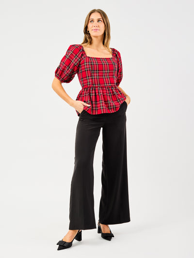 Woman wearing a red plaid top and black pants on a white background