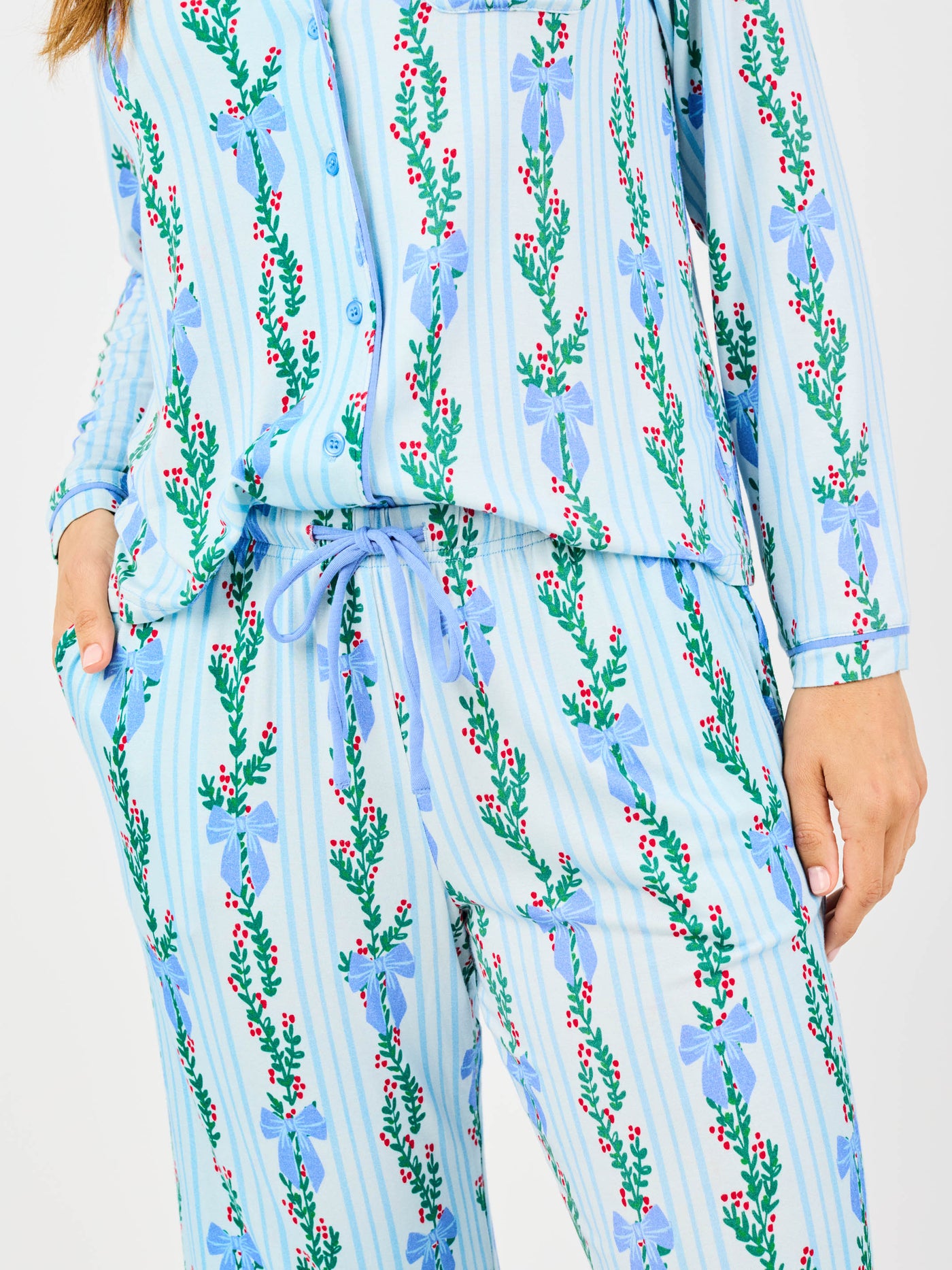 Woman wearing a blue holiday floral bow pattern pajama set on a white background