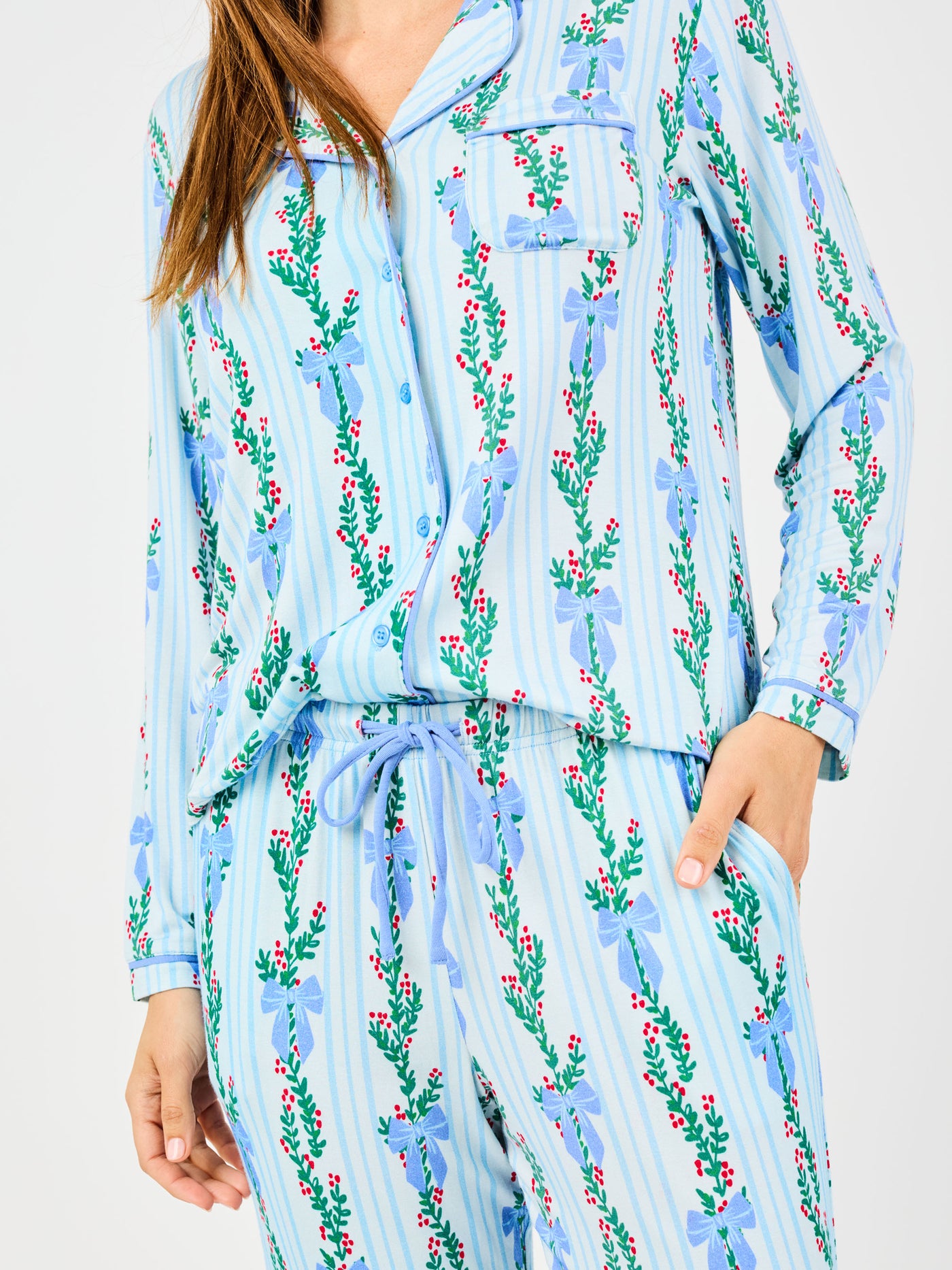 Woman wearing a blue holiday floral bow pattern pajama set on a white background