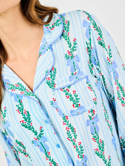 Woman wearing a blue holiday floral bow pattern pajama set on a white background