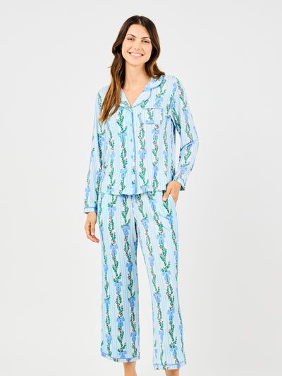 Woman wearing a blue holiday floral bow pattern pajama set on a white background