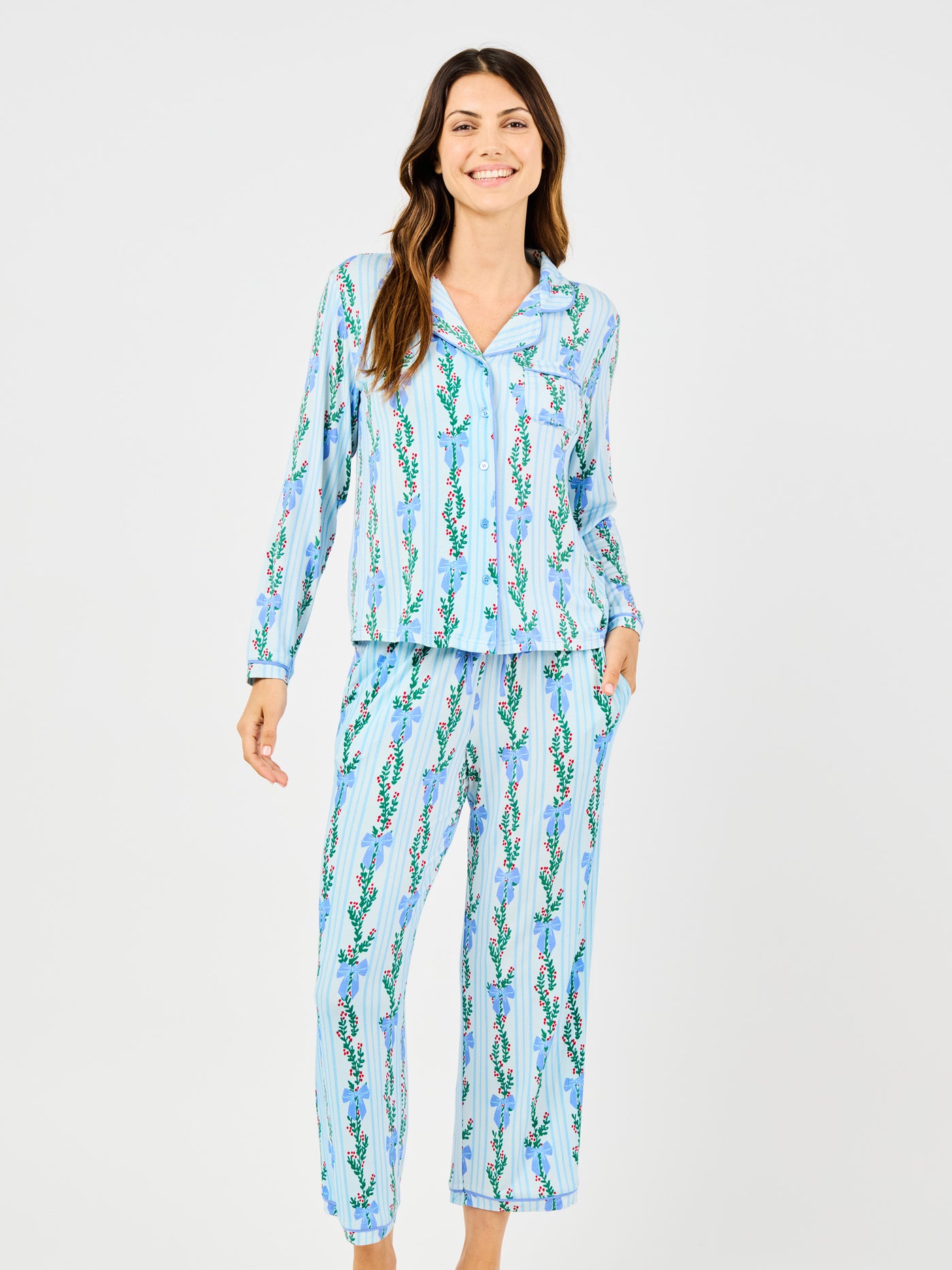Woman wearing a blue holiday floral bow pattern pajama set on a white background