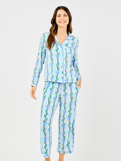 Woman wearing a blue holiday floral bow pattern pajama set on a white background