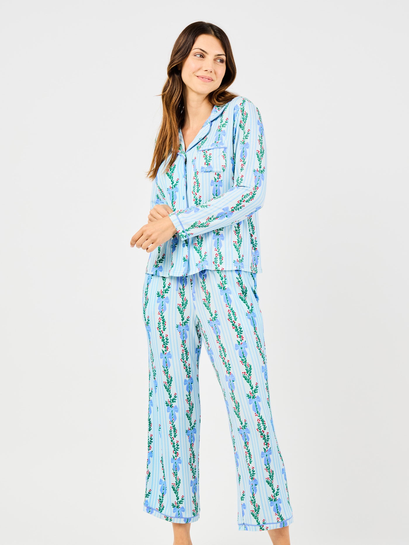 Woman wearing a blue holiday floral bow pattern pajama set on a white background