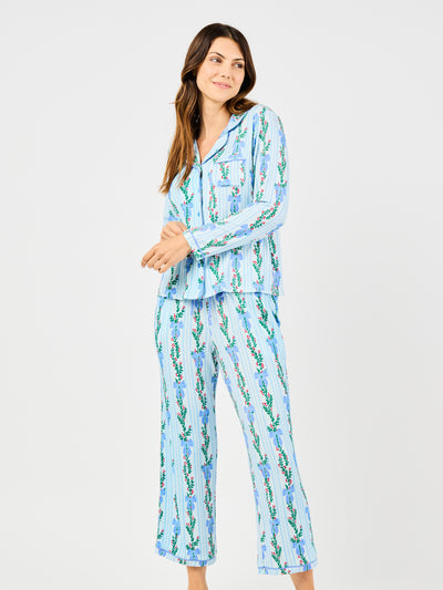 Woman wearing a blue holiday floral bow pattern pajama set on a white background