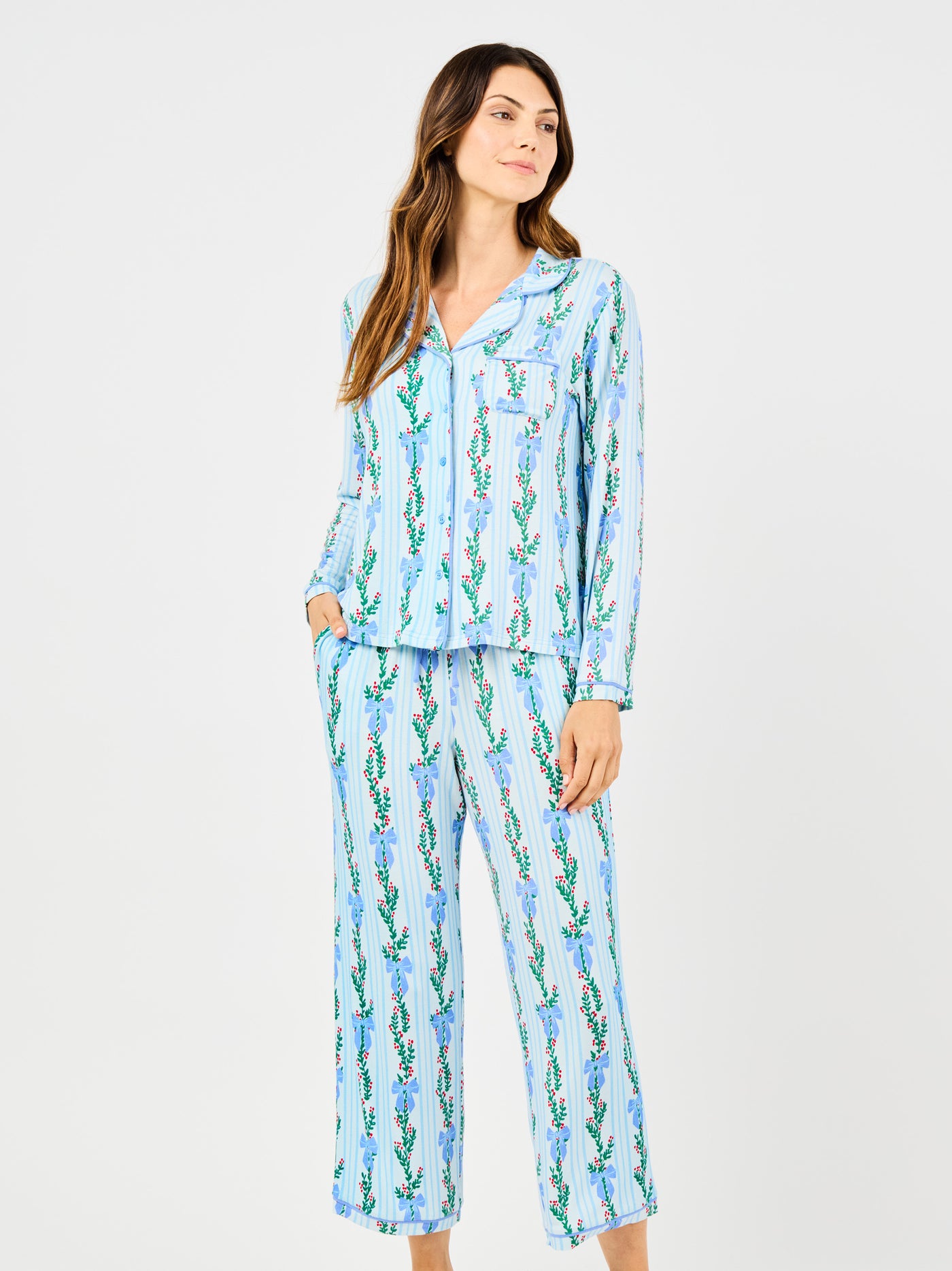 Woman wearing a blue holiday floral bow pattern pajama set on a white background