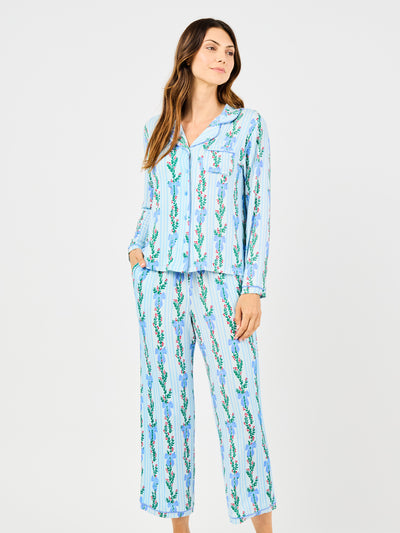 Woman wearing a blue holiday floral bow pattern pajama set on a white background
