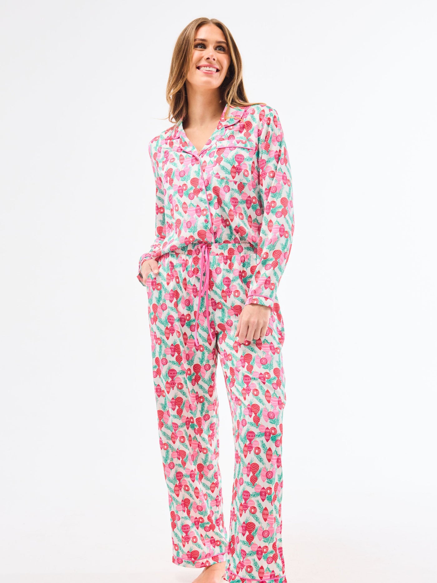 Woman wearing a christmas pajama set  with holiday ornaments in pinks, greens and reds on a white background