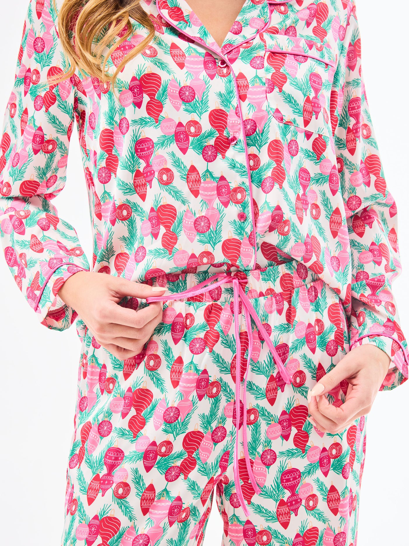 Woman wearing a christmas pajama set  with holiday ornaments in pinks, greens and reds on a white background
