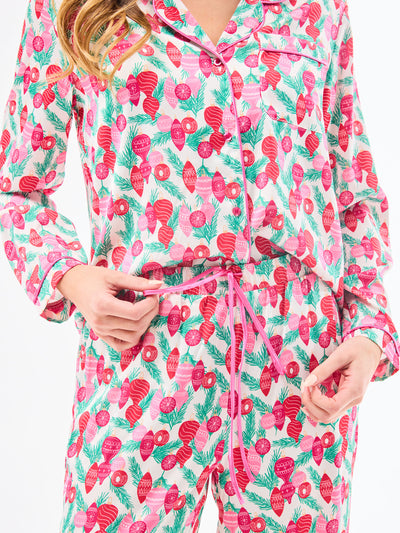 Woman wearing a christmas pajama set  with holiday ornaments in pinks, greens and reds on a white background