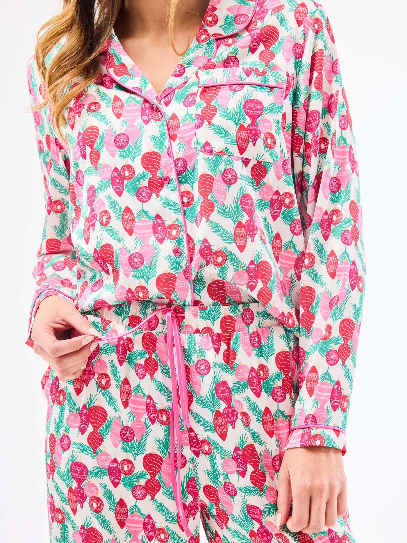Woman wearing a christmas pajama set  with holiday ornaments in pinks, greens and reds on a white background