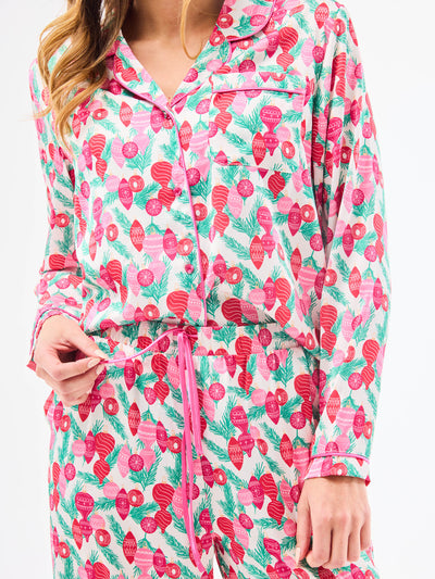 Woman wearing a christmas pajama set  with holiday ornaments in pinks, greens and reds on a white background