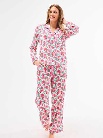 Woman wearing a christmas pajama set  with holiday ornaments in pinks, greens and reds on a white background