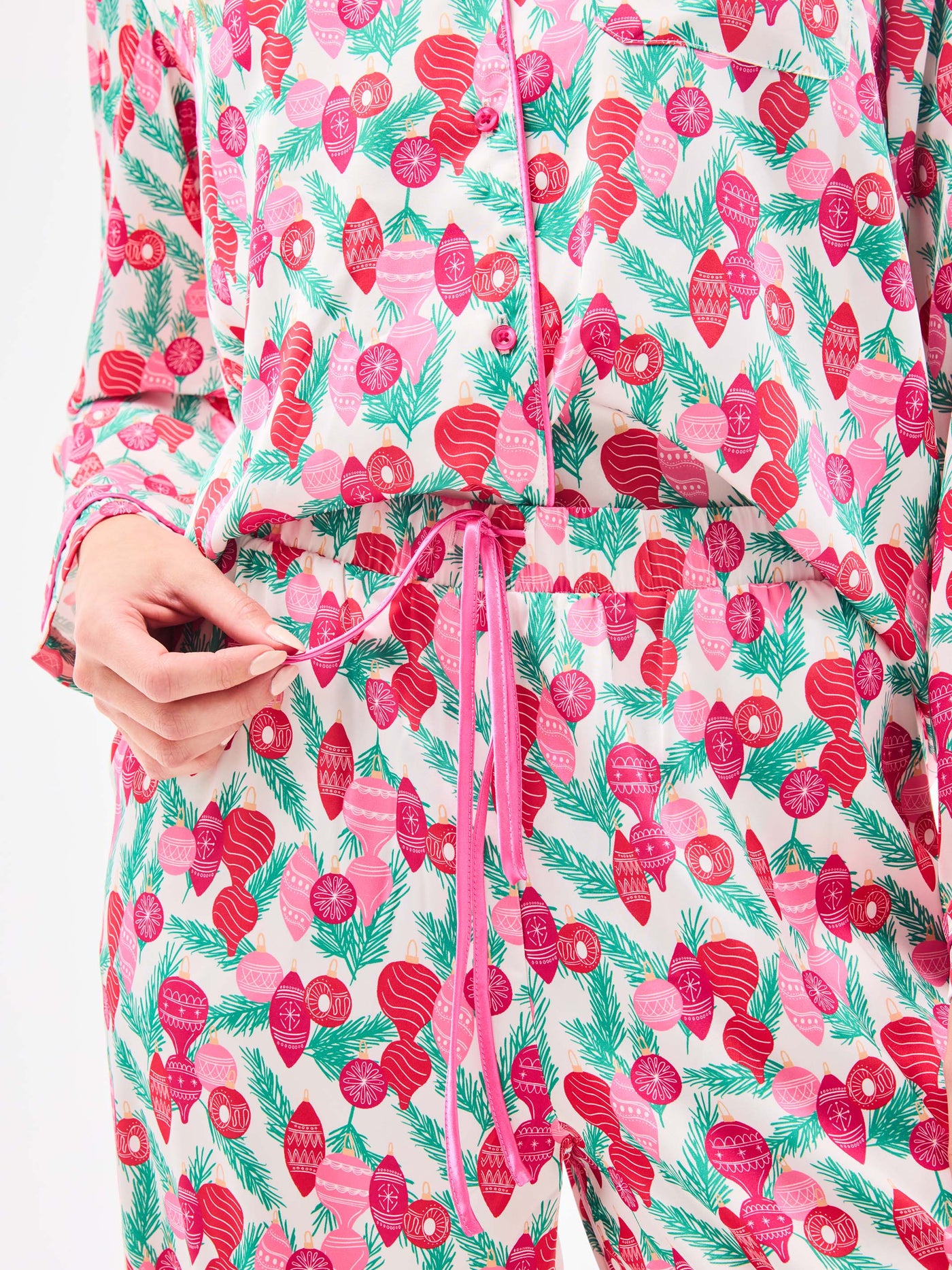 Woman wearing a christmas pajama set  with holiday ornaments in pinks, greens and reds on a white background