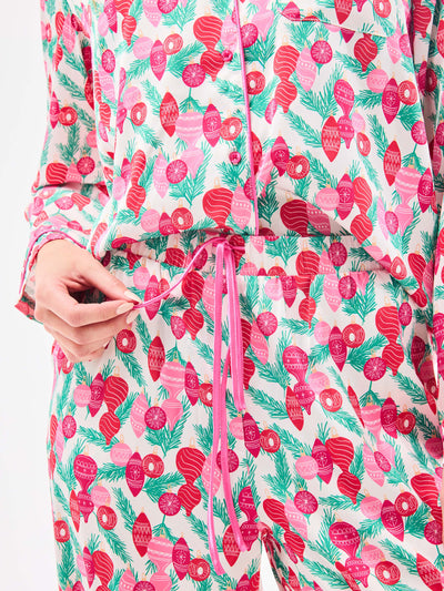Woman wearing a christmas pajama set  with holiday ornaments in pinks, greens and reds on a white background