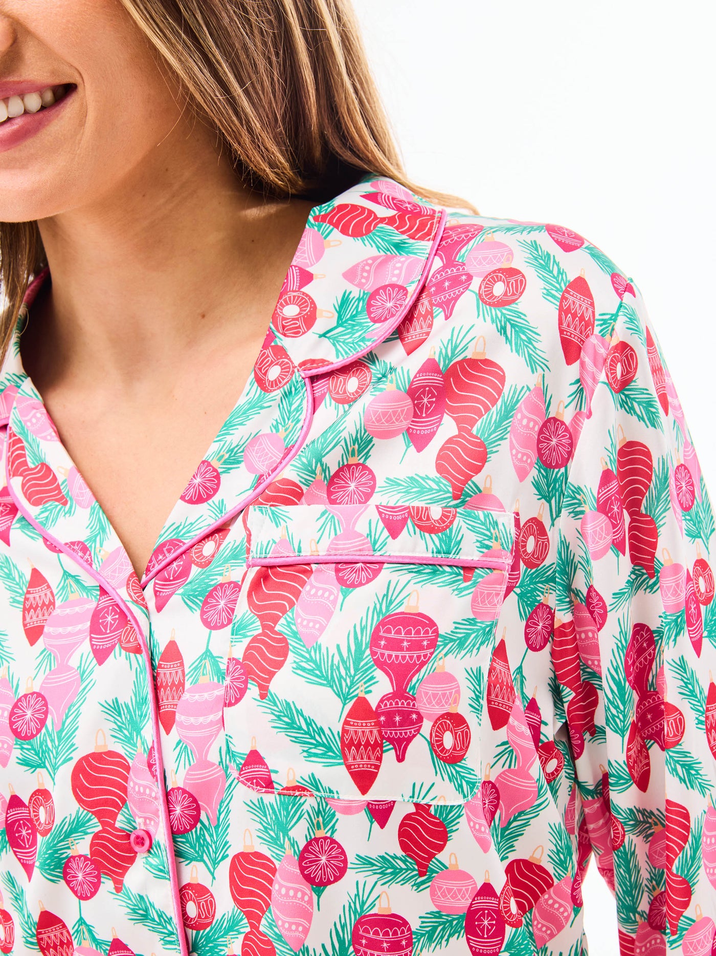 Woman wearing a christmas pajama set  with holiday ornaments in pinks, greens and reds on a white background