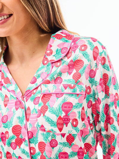 Woman wearing a christmas pajama set  with holiday ornaments in pinks, greens and reds on a white background