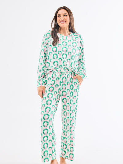 Woman wearing a green and pink patterned pajamas that feature christmas wreaths with pink bows on themon a white background