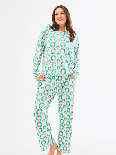 Woman wearing a green and pink patterned pajamas that feature christmas wreaths with pink bows on themon a white background