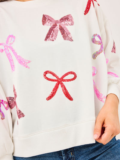 Close-up of a white sweater with pink and red bow patterns.