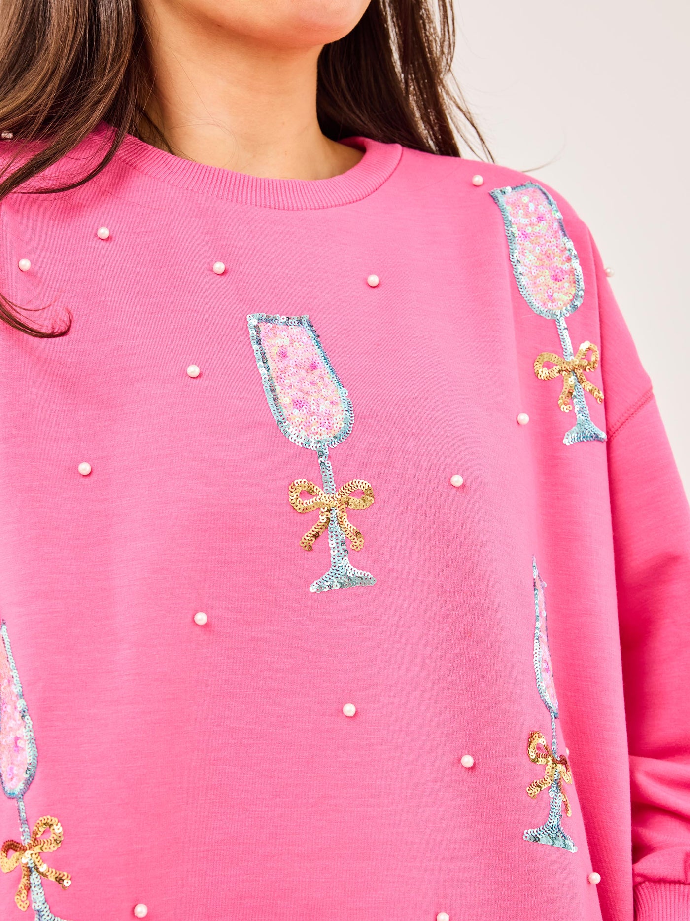 Pink sweatshirt with champagne glass and bow designs on a white background
