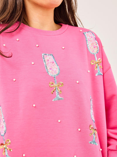 Pink sweatshirt with champagne glass and bow designs on a white background