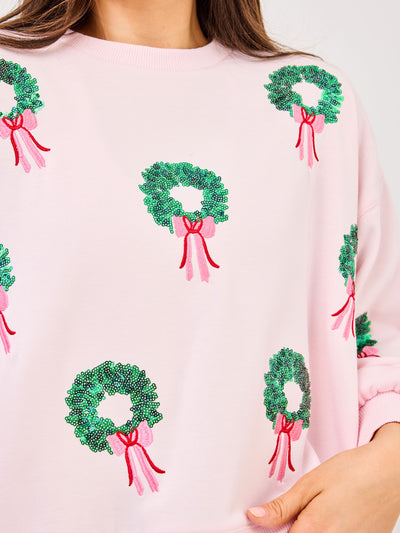 Pink sweater with green wreath and red and pink bow patterns on a white background