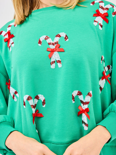 Woman wearing a green sweatshirt with candy cane patterns and blue jeans on a white background