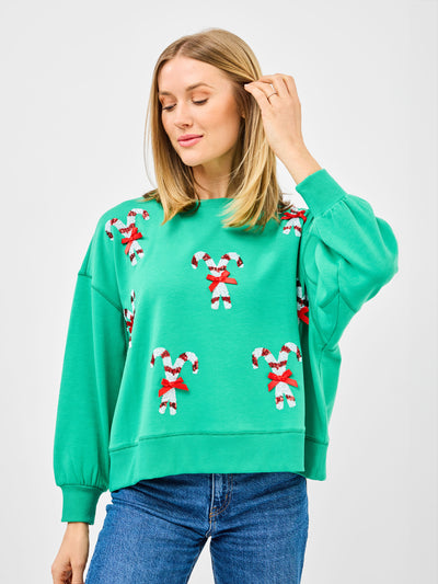 Woman wearing a green sweatshirt with candy cane patterns and blue jeans on a white background