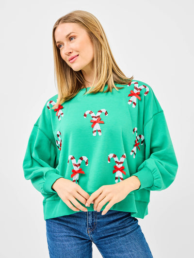 Woman wearing a green sweatshirt with candy cane patterns and blue jeans on a white background