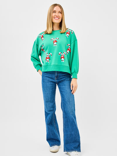 Woman wearing a green sweatshirt with candy cane patterns and blue jeans on a white background