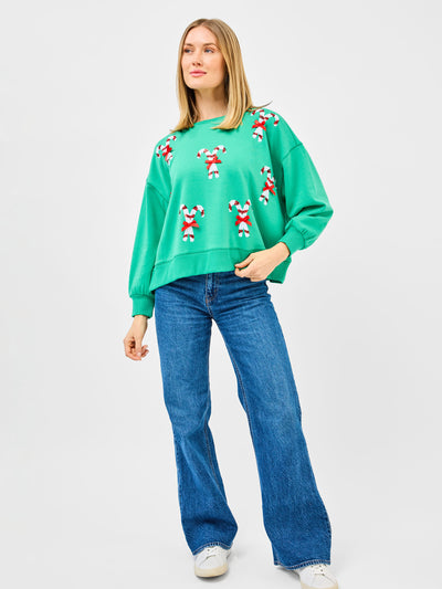 Woman wearing a green sweatshirt with candy cane patterns and blue jeans on a white background