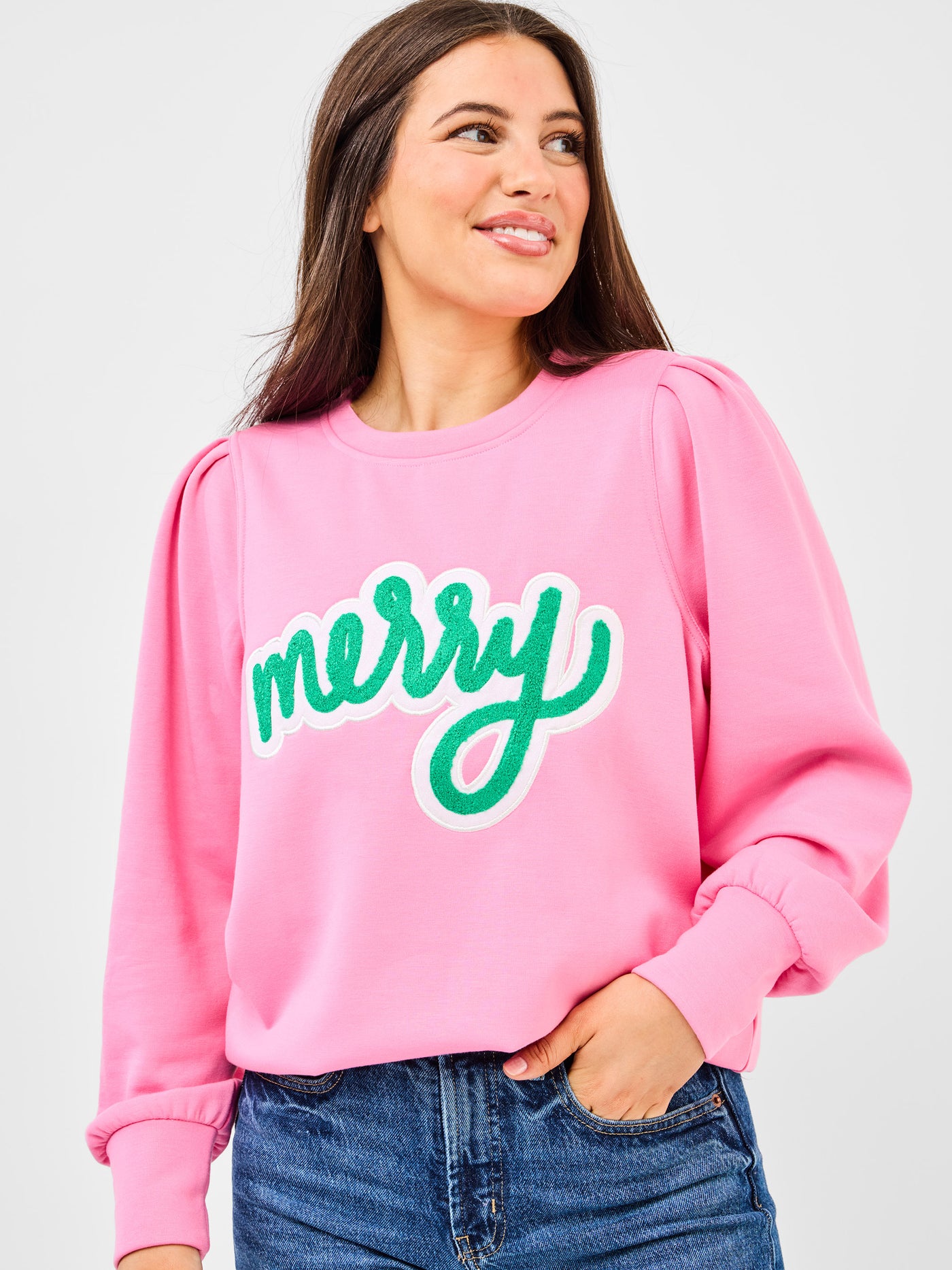 Person wearing a pink sweatshirt with 'merry' in green text on a plain background