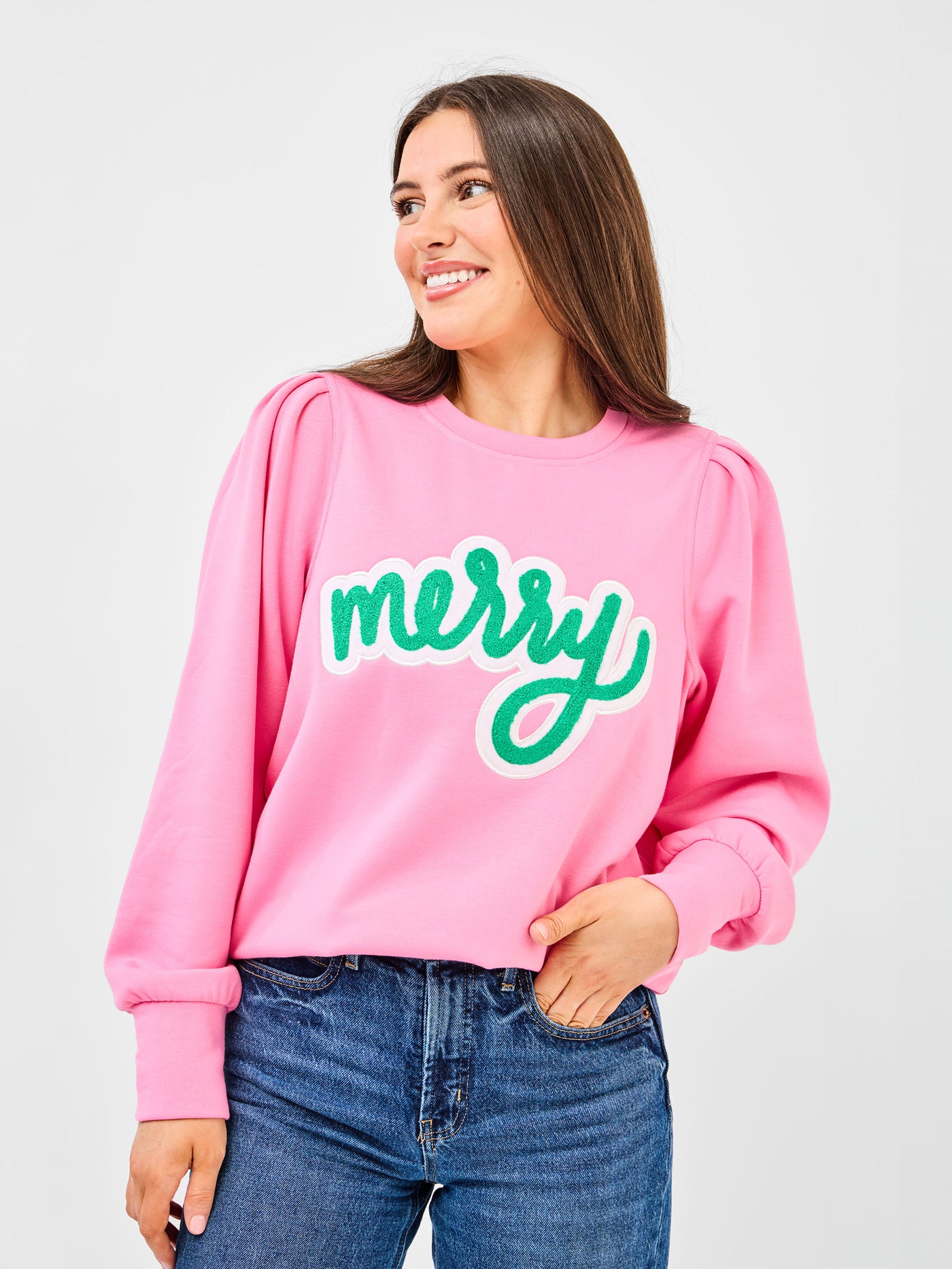 Person wearing a pink sweatshirt with 'merry' in green text on a plain background