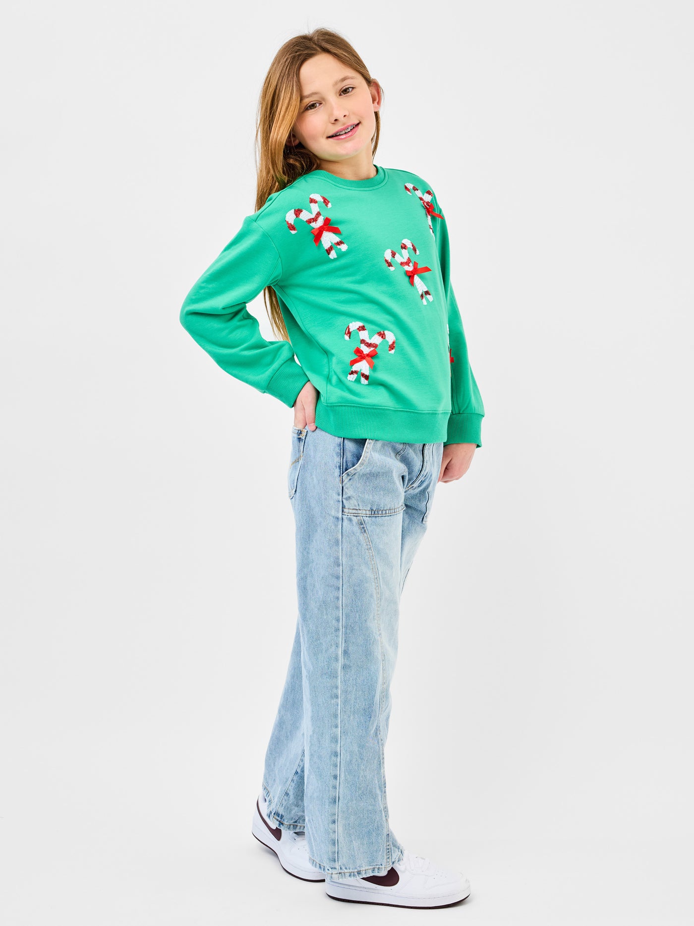 Young pre-teen girl wearing a green sweatshirt with candy cane designs on a white background