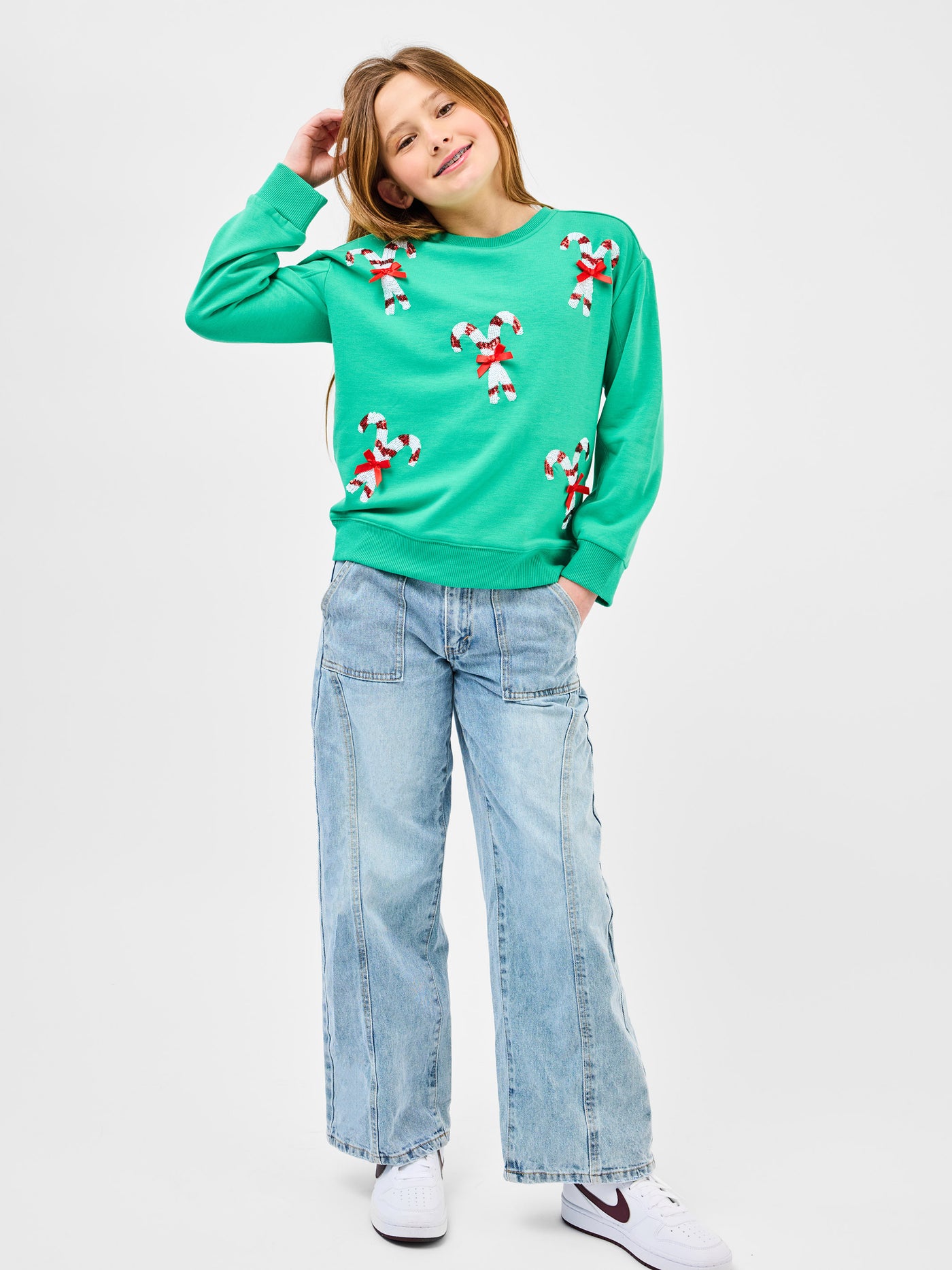 Young pre-teen girl wearing a green sweatshirt with candy cane designs on a white background