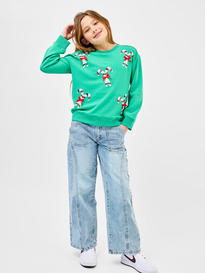 Young pre-teen girl wearing a green sweatshirt with candy cane designs on a white background