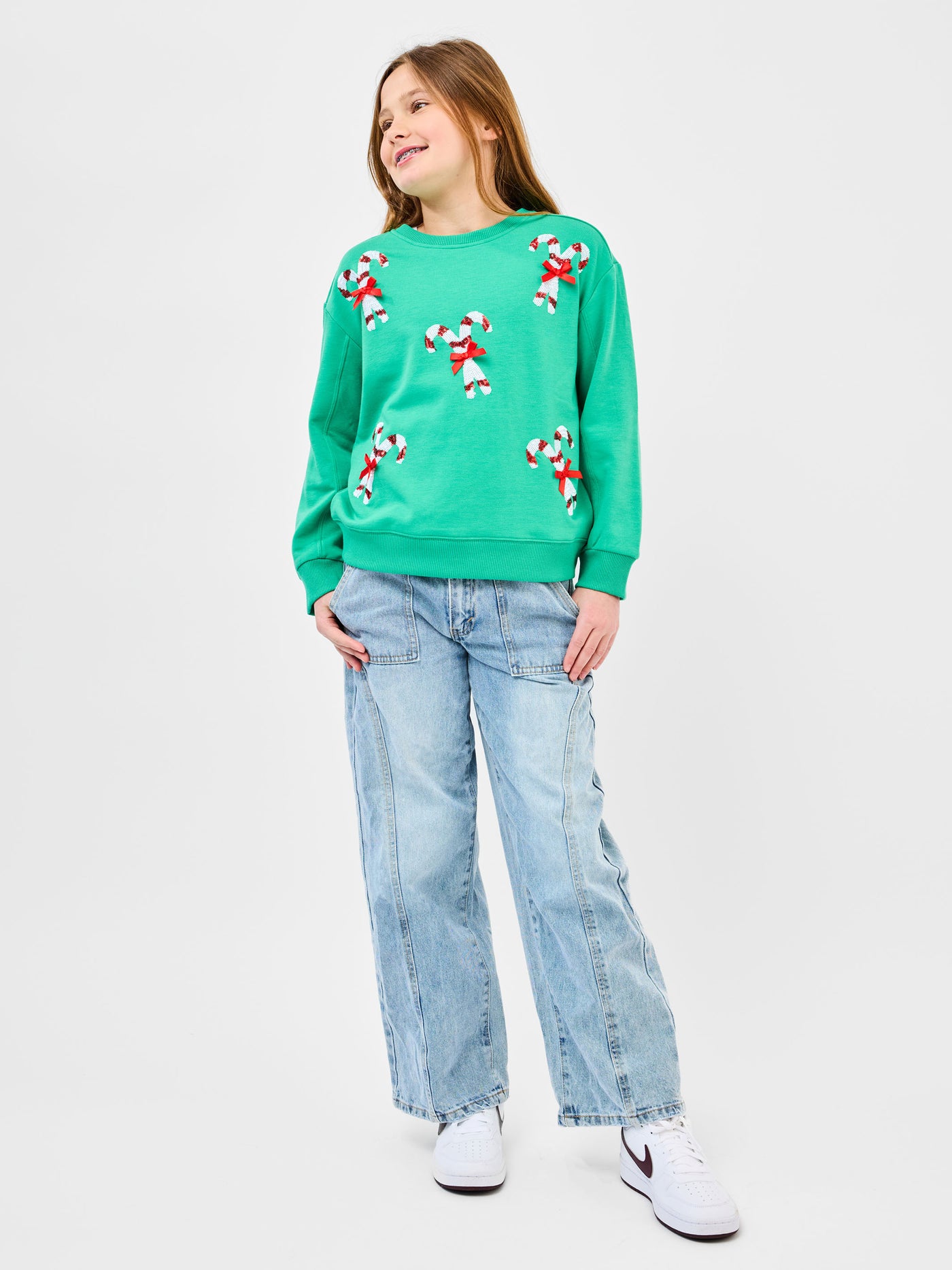 Young pre-teen girl wearing a green sweatshirt with candy cane designs on a white background