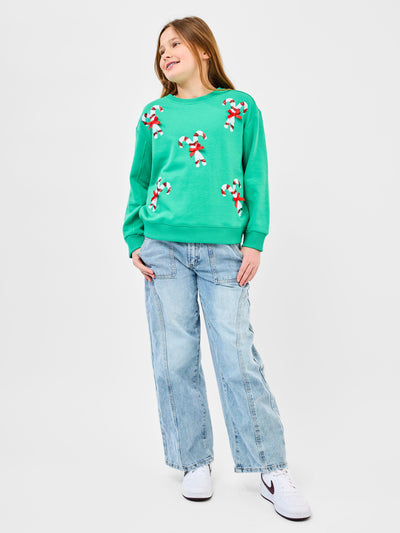 Young pre-teen girl wearing a green sweatshirt with candy cane designs on a white background