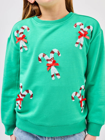Young pre-teen girl wearing a green sweatshirt with candy cane designs on a white background