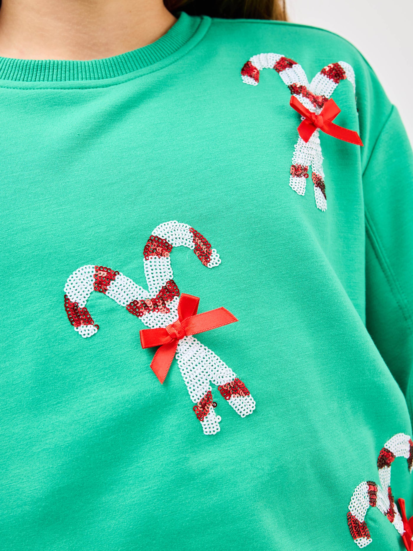 Young pre-teen girl wearing a green sweatshirt with candy cane designs on a white background