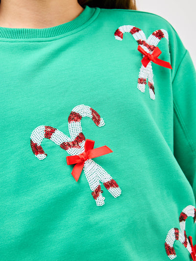 Young pre-teen girl wearing a green sweatshirt with candy cane designs on a white background