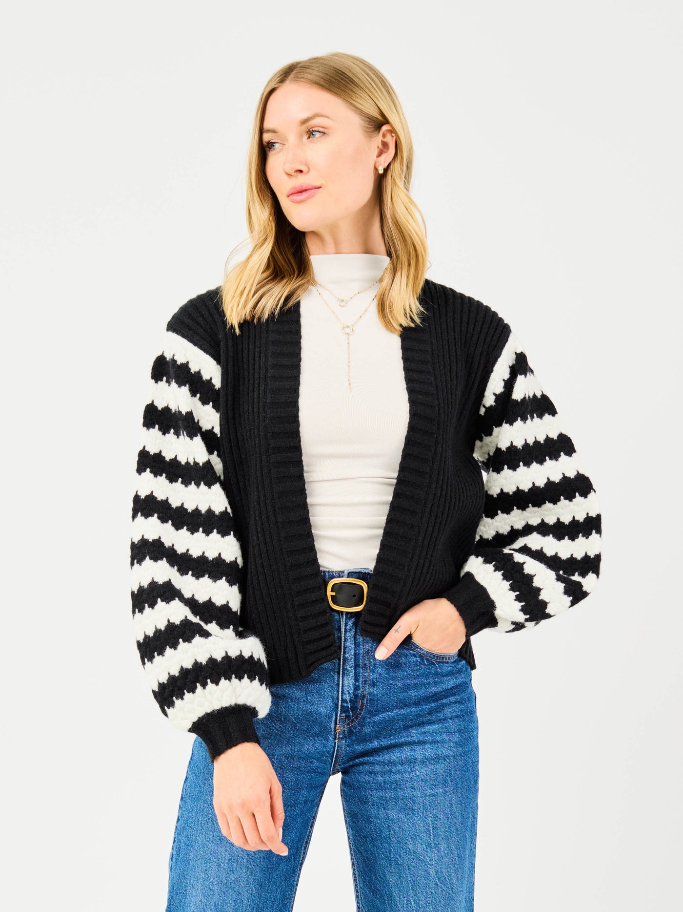 Woman wearing a black and white striped cardigan with blue jeans on a light gray background