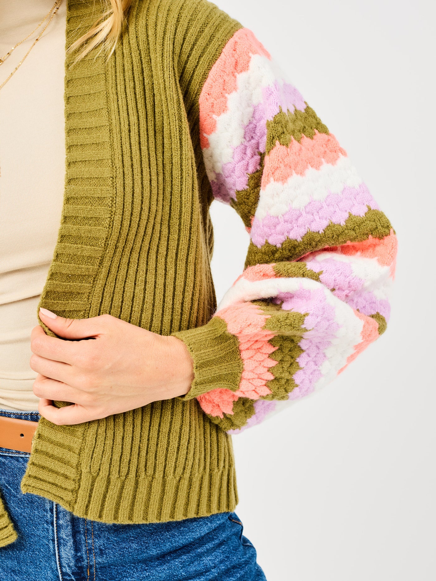 Person wearing a green sweater with colorful sleeves on a plain background