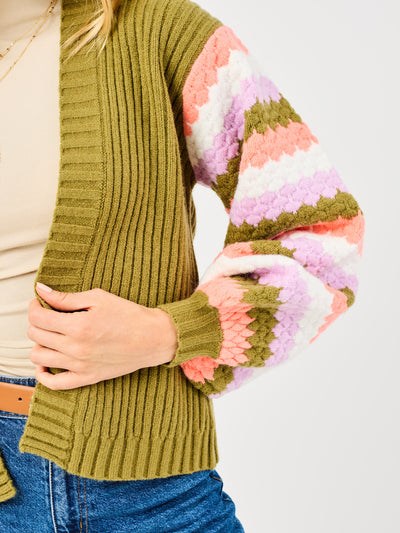 Person wearing a green sweater with colorful sleeves on a plain background