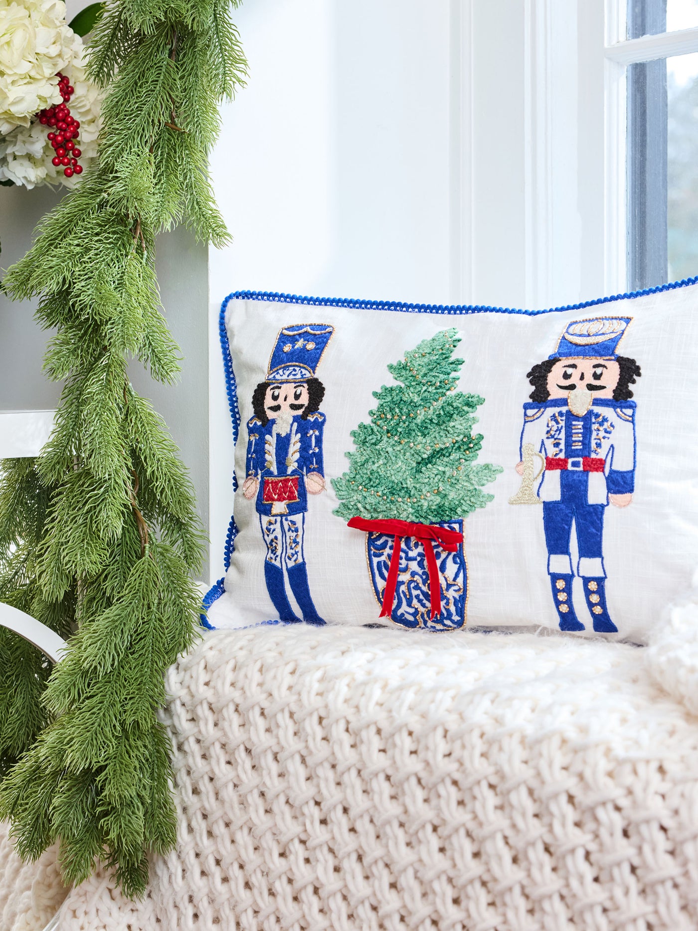 Decorative pillow with nutcracker design on a white surface with greenery.