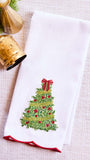 White towel with Christmas tree design and red trim, placed on a textured surface with decorative elements.