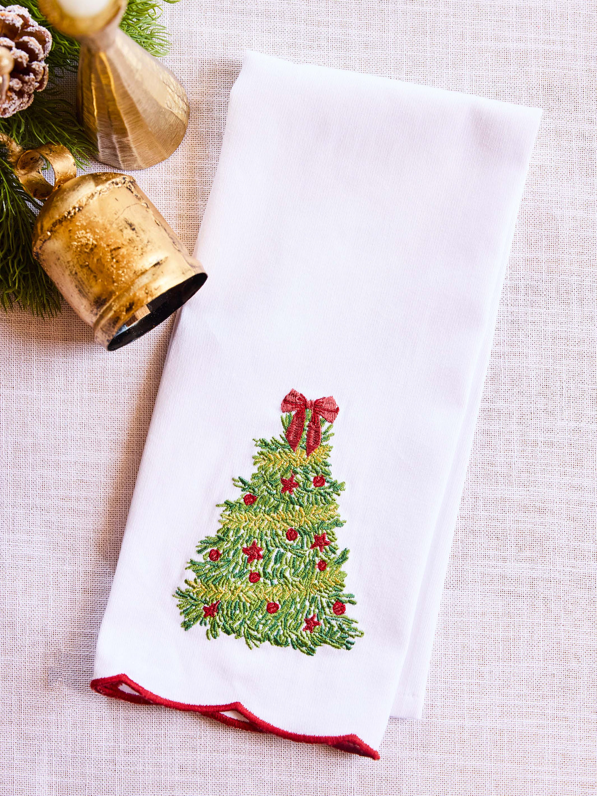 White towel with Christmas tree design and red trim, placed on a textured surface with decorative elements.